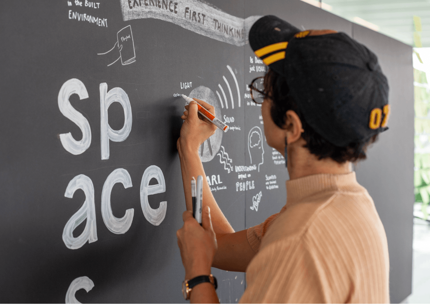 Person writing on a chalkboard, illustrating concepts related to space, light, and sound in architectural design.