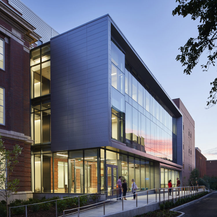 North facade of Troy Hall with glass box atrium and students gathered in front of doors along sidewalk.