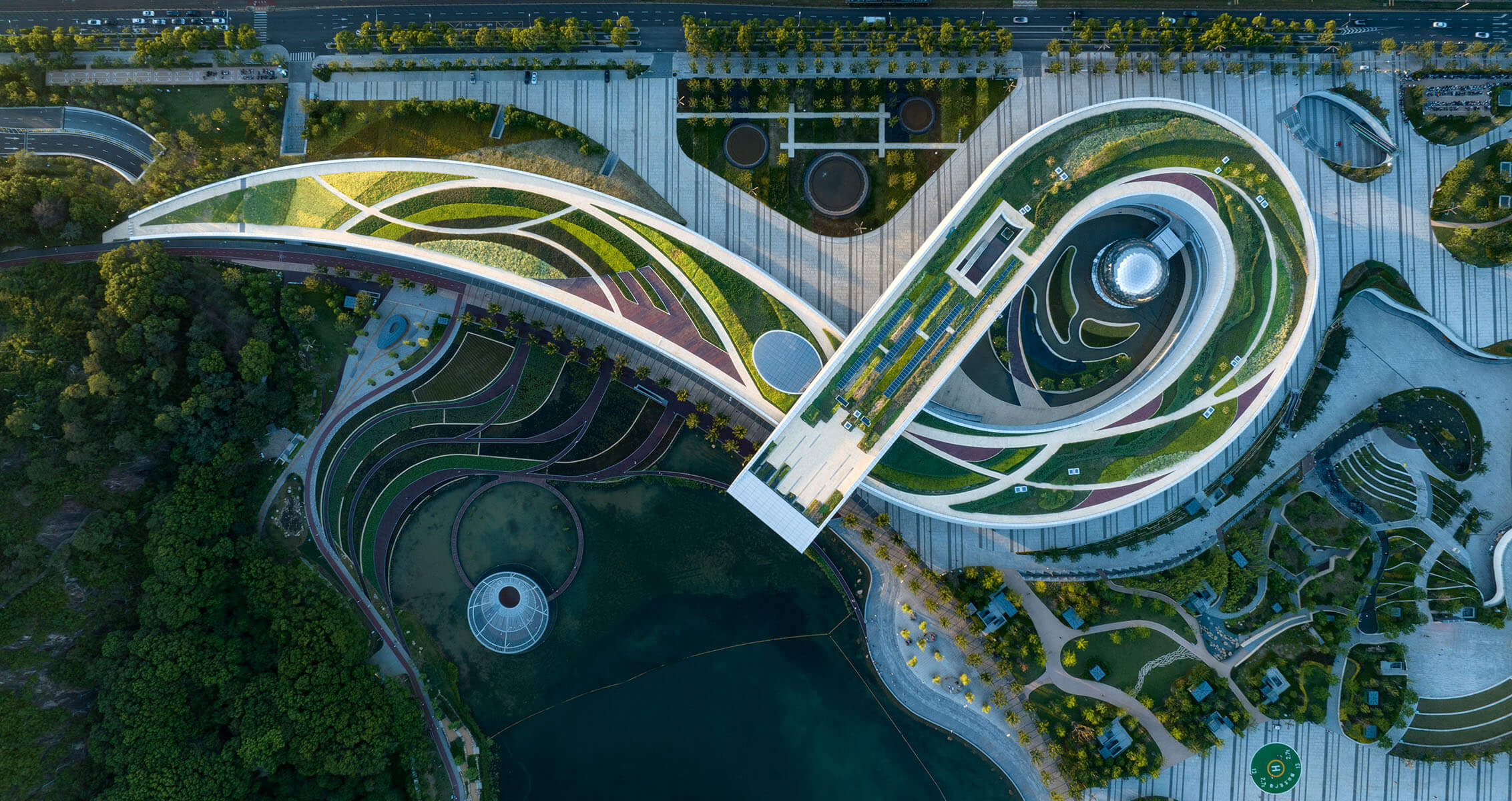 Aerial view of a landscaped area featuring winding pathways, green roofs, water features, and surrounding greenery. Ideal for urban exploration.