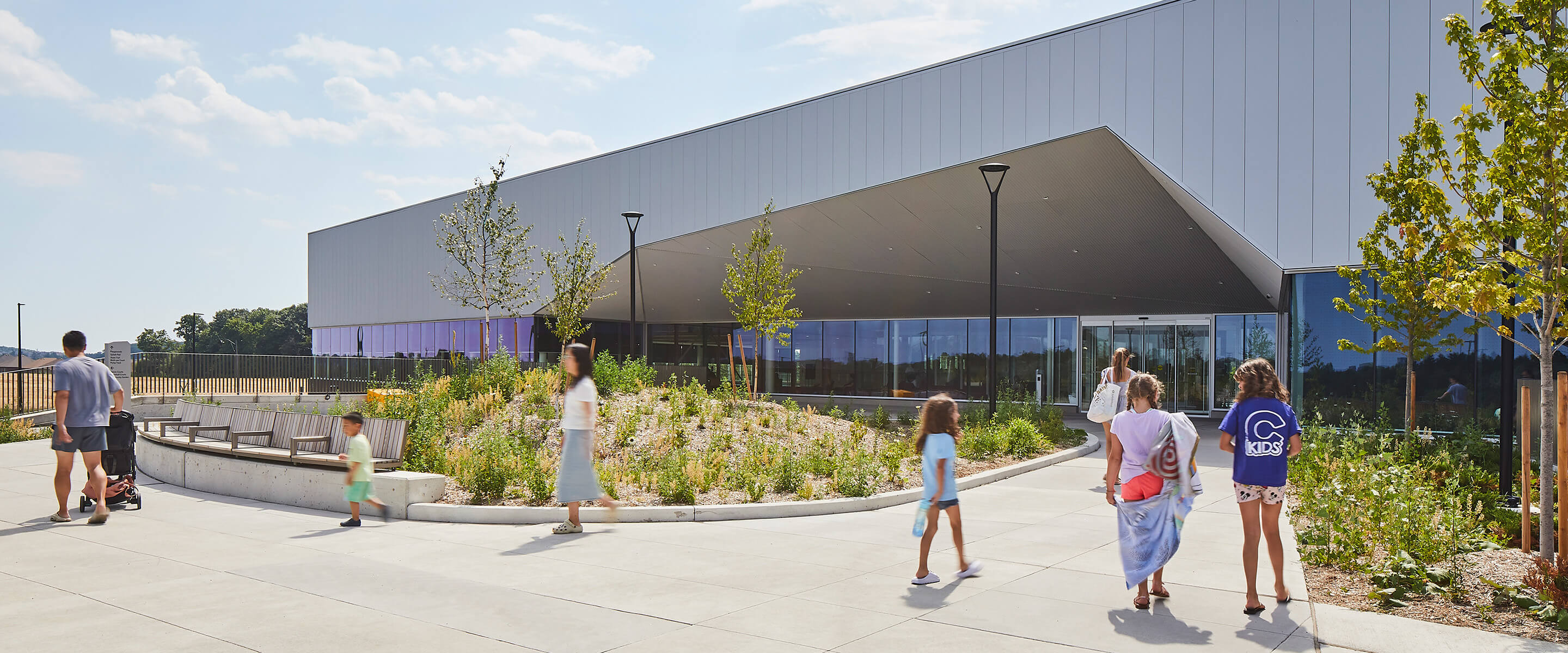 Modern community center exterior with people walking, plants, and clear blue sky.