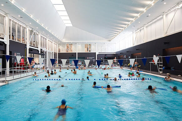 People swimming in an indoor pool with lanes and a modern design.