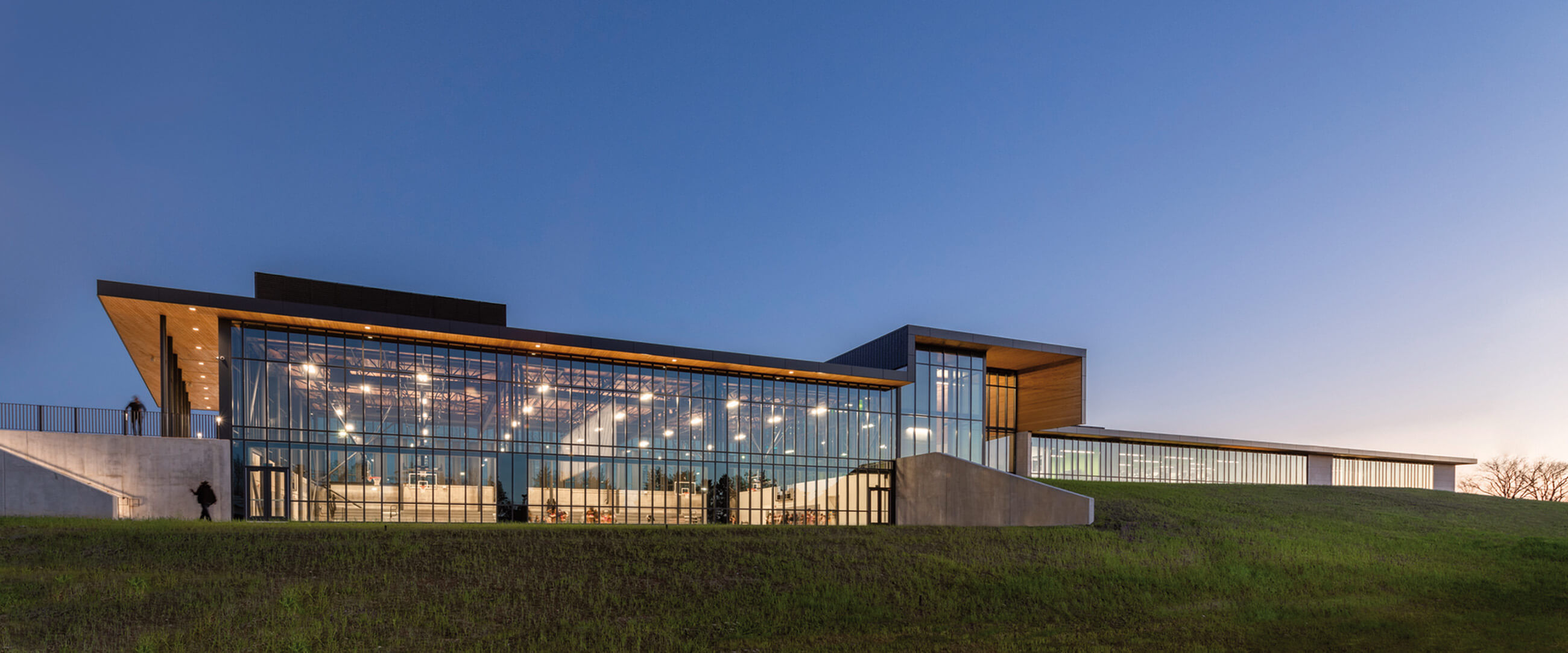 Modern glass building at twilight with green landscape.