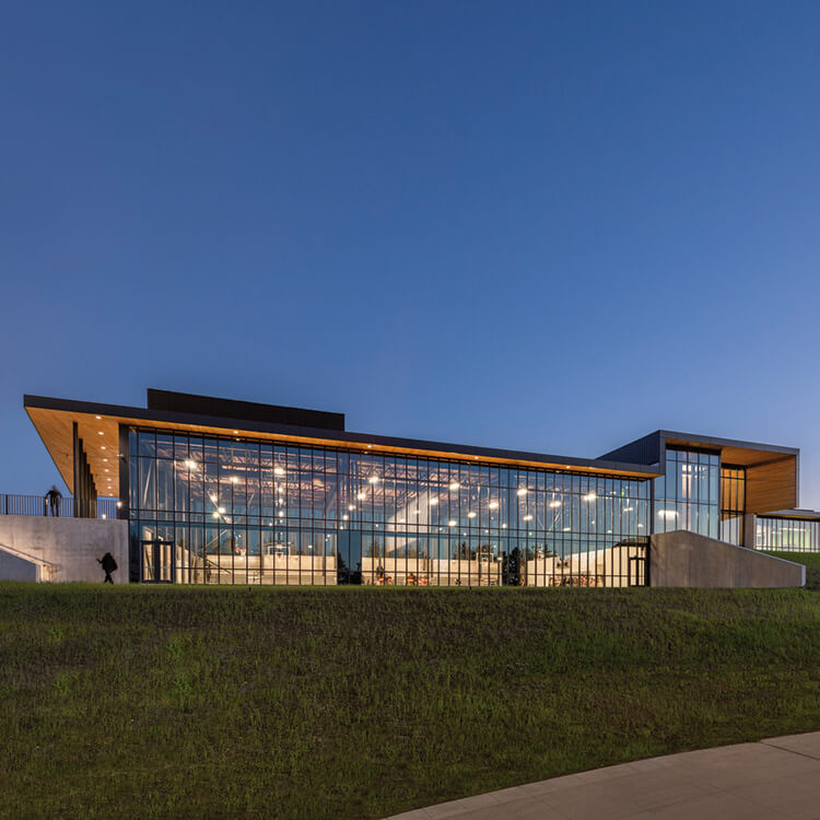 Modern glass building at dusk with illuminated interior.