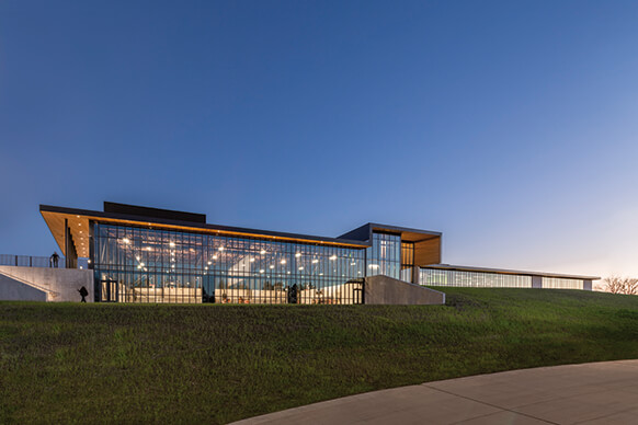 Modern glass building at dusk with illuminated interior and clear sky.