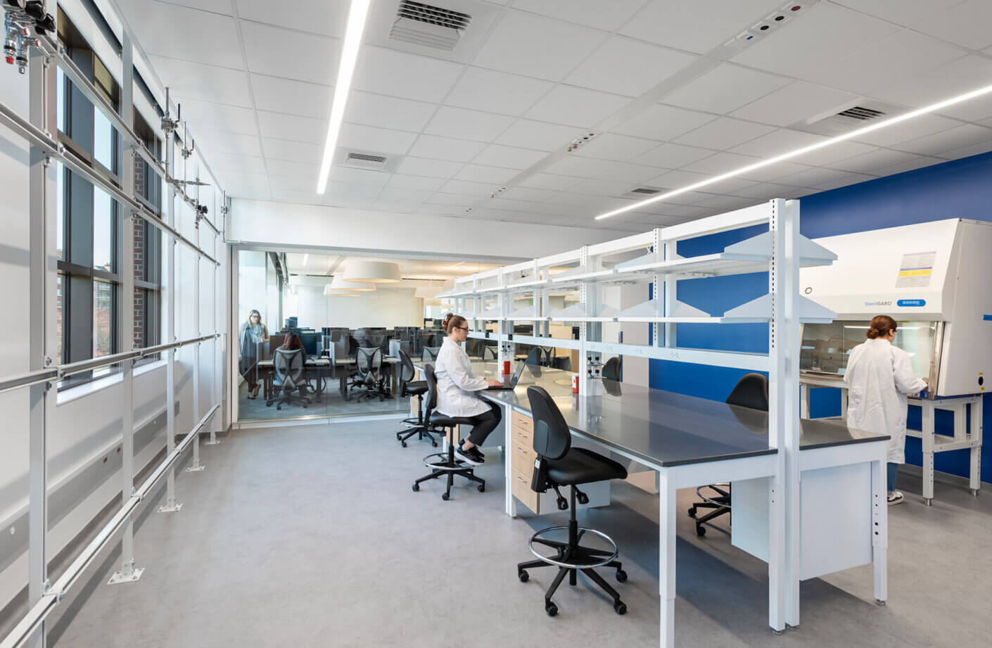 Lab space with people working and view through glass wall to office workstations