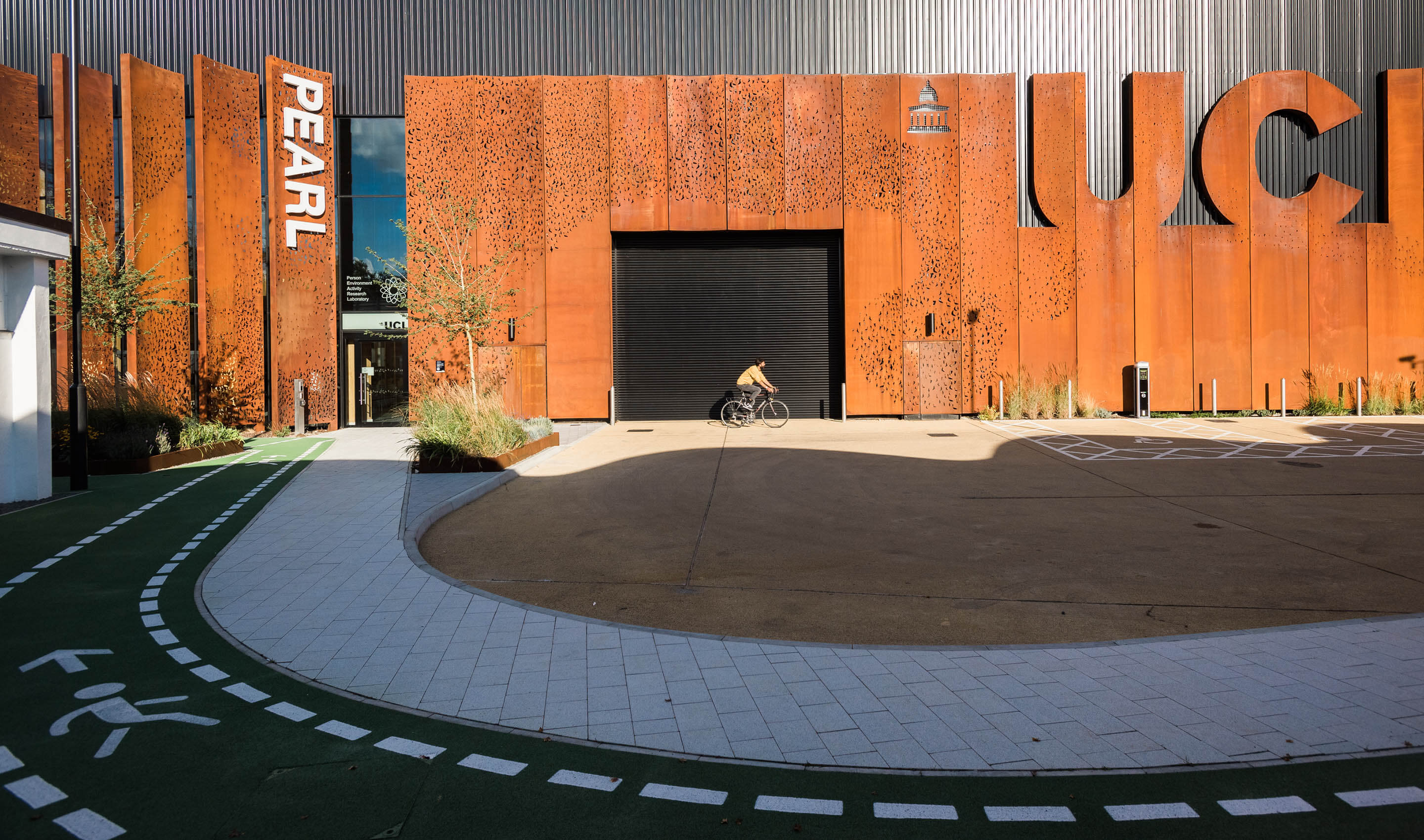 Photo of PEARL, the Person-Environment-Activity Research Laboratory, showing a bicyclist and a paved, marked pathway to the building entrance