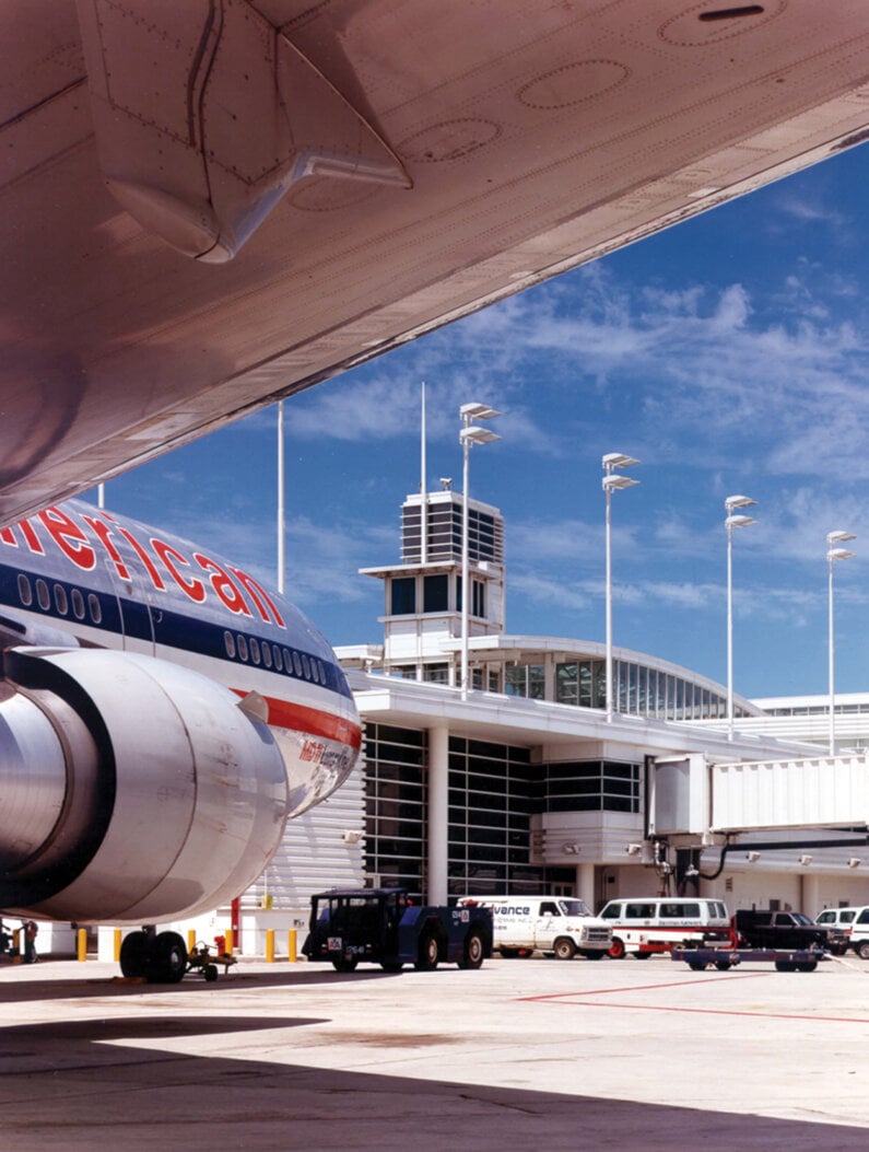 Photograph view of air control tower rising from Terminal D building from under the wing of an airplane