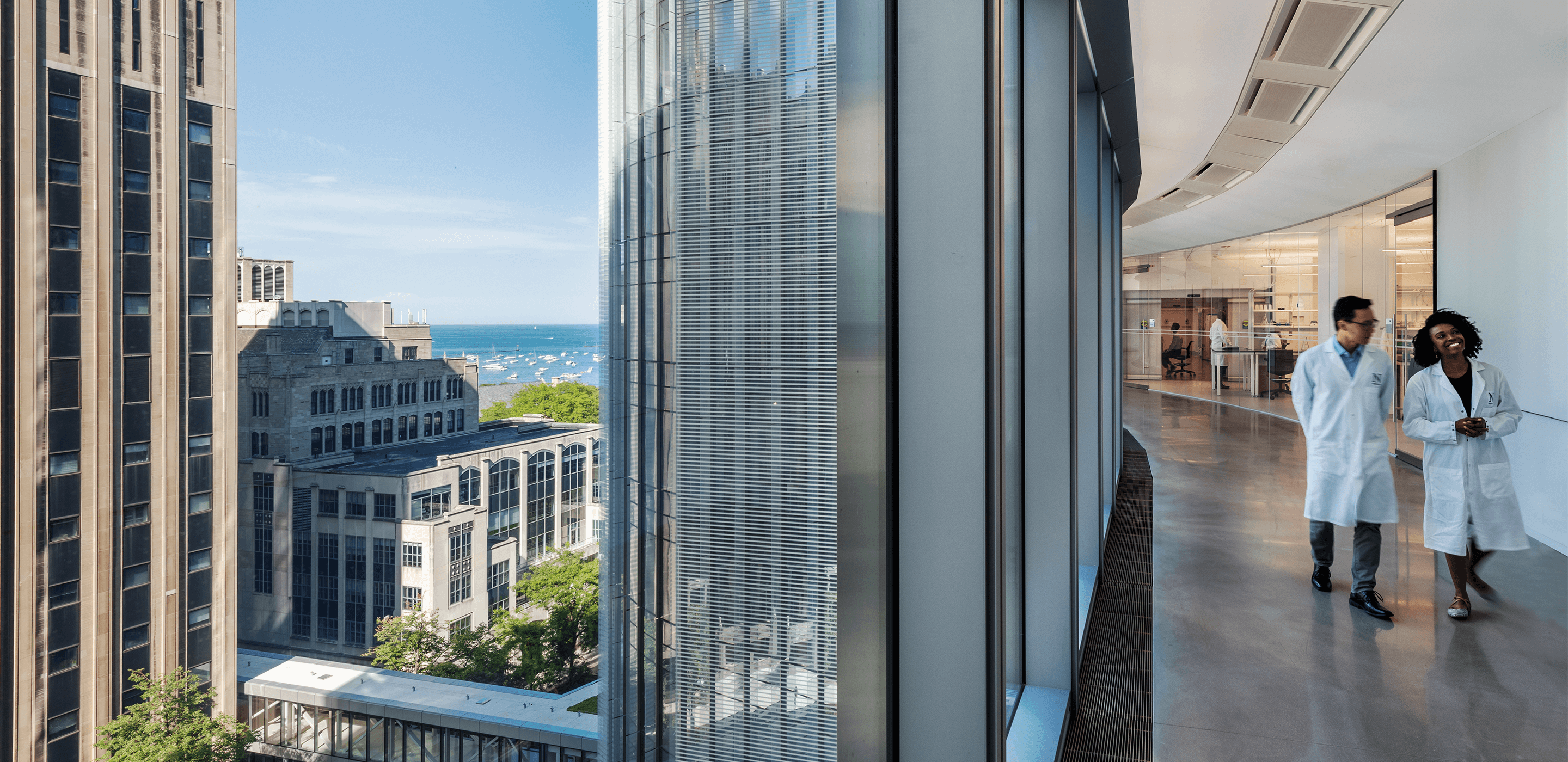 Photo showing researchers walking in an upper-story corridor with a view outside the lab of Lake Michigan and downtown Chicago