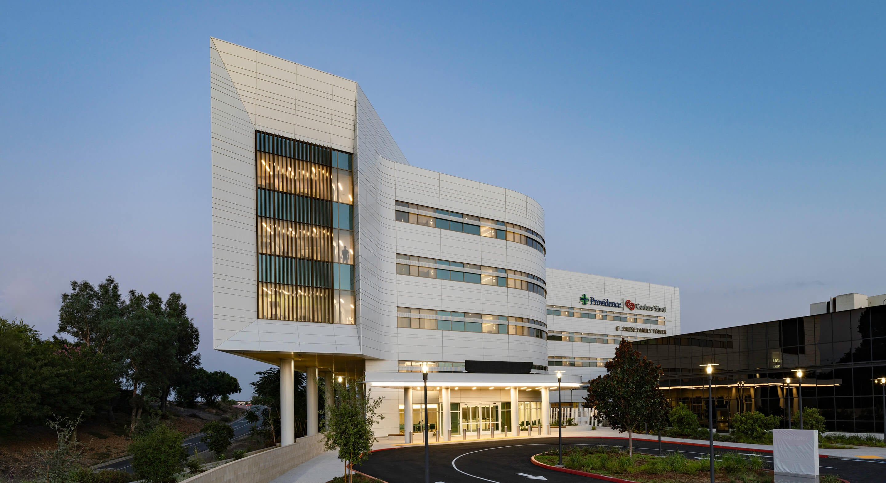 Modern hospital building exterior at dusk with clear sky and trees.