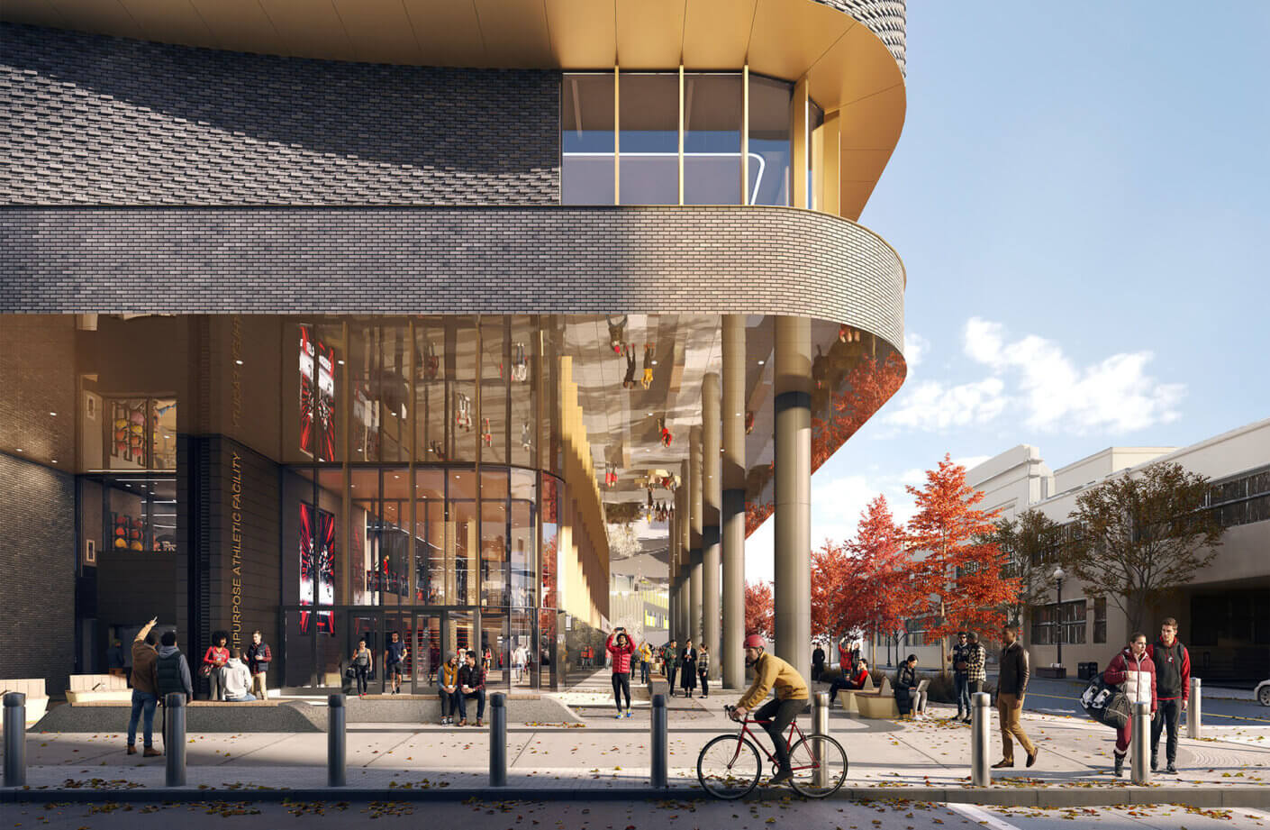 View of a multi-purpose athletic facility with large windows, outdoor seating, and bicycle access, surrounded by trees and pedestrians.