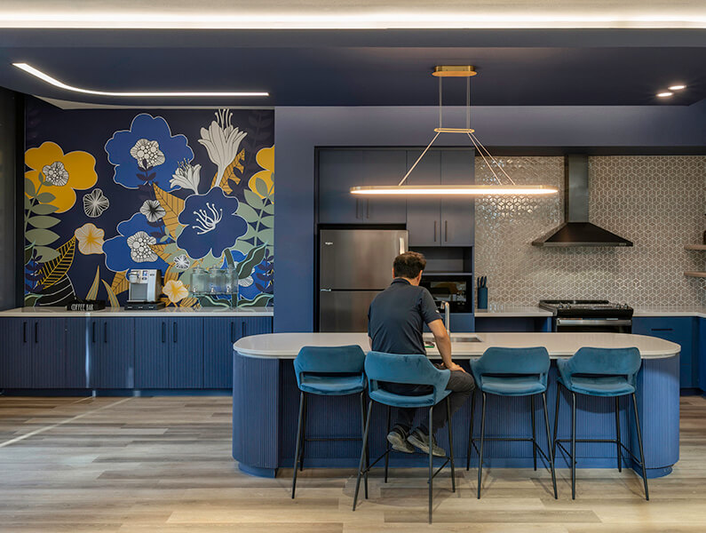 A man sits in Oak Lawn Place's navy blue community dining space by a floral mural