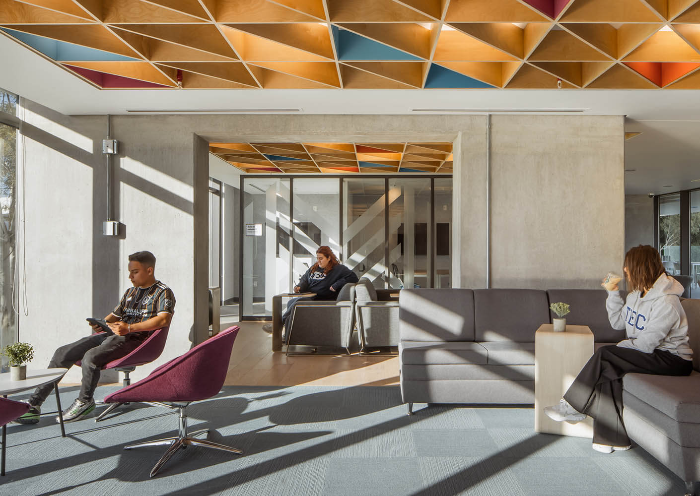 A common space with students in the sunlit interior of the residence hall, featuring a colorful wooden ceiling