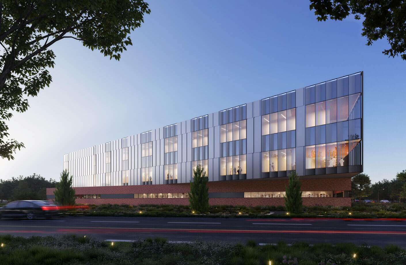 Exterior view of a research building featuring glass facade and brick base, surrounded by landscaping and a road with passing vehicles at dusk.