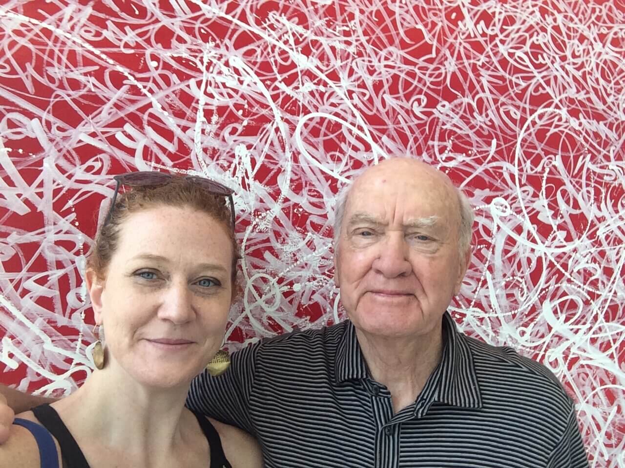 Photo of a woman and her father in front of a red patterned wall