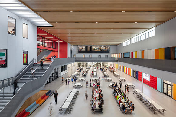 Modern school cafeteria and atrium with students, vibrant colors, and natural light from multiple directions.