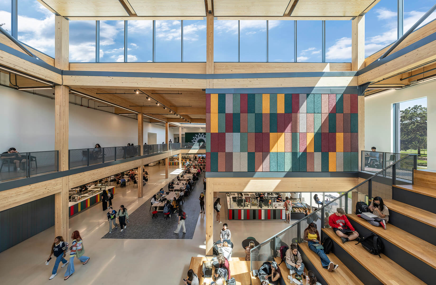 Modern college atrium with students studying, featuring colorful wall panels and open seating areas.