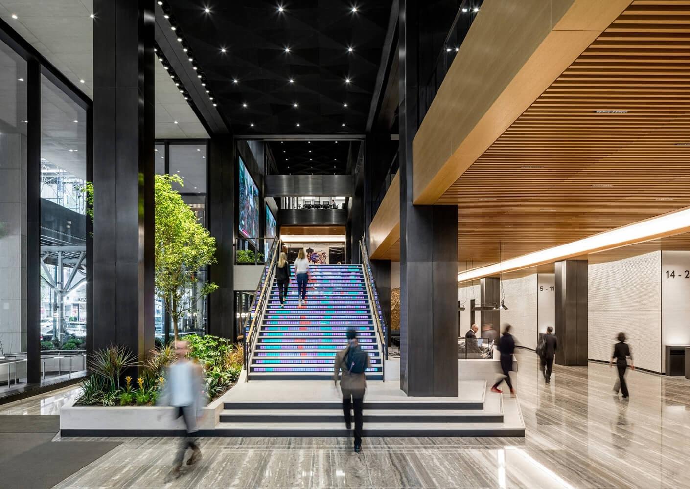 Modern office lobby with colorful digital staircase, sleek design, and people walking.