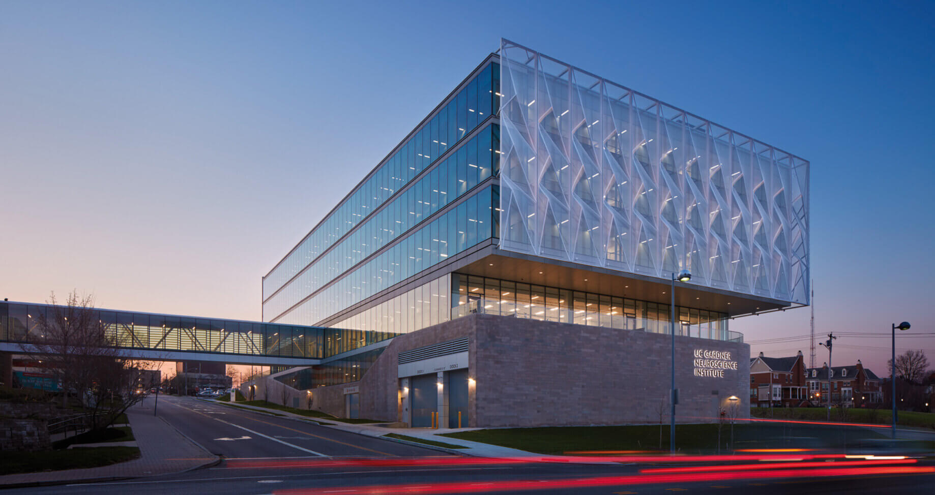 Modern glass building at dusk with bridge connecting over street.