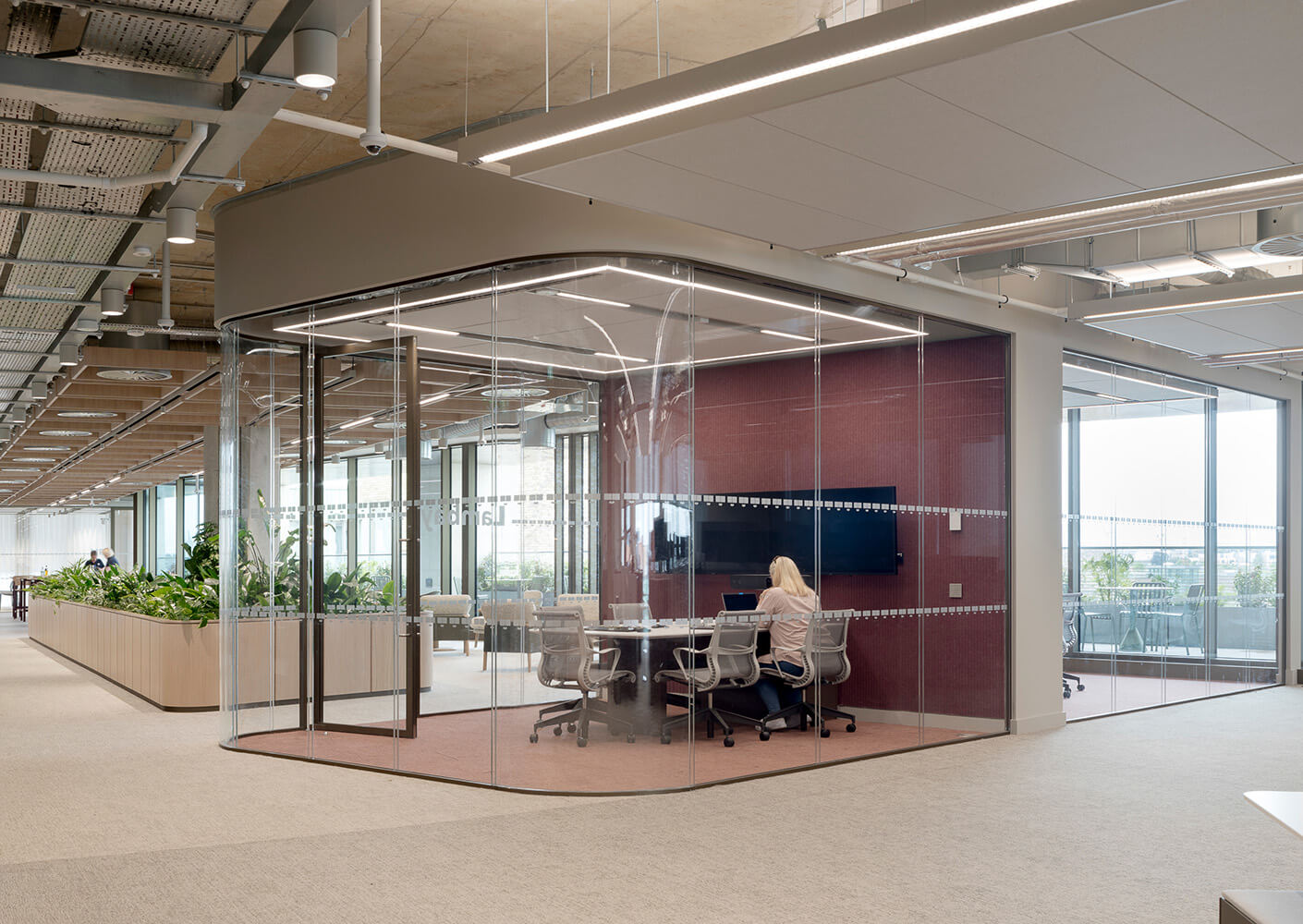 Modern office meeting room with glass walls and a person working on a laptop.