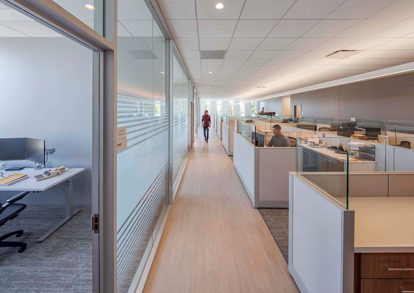 Modern office corridor with cubicles and a person walking.