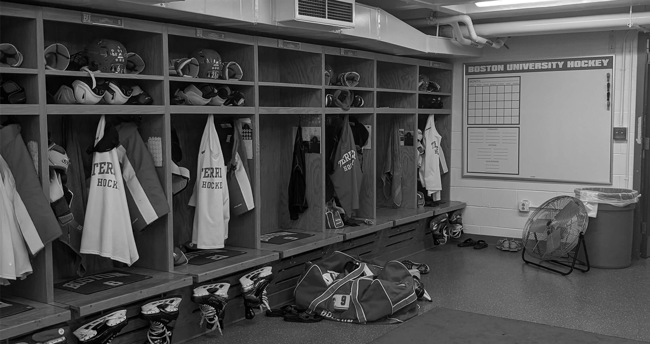 Existing conditions of Boston University women's ice hockey locker room with gear and uniforms.