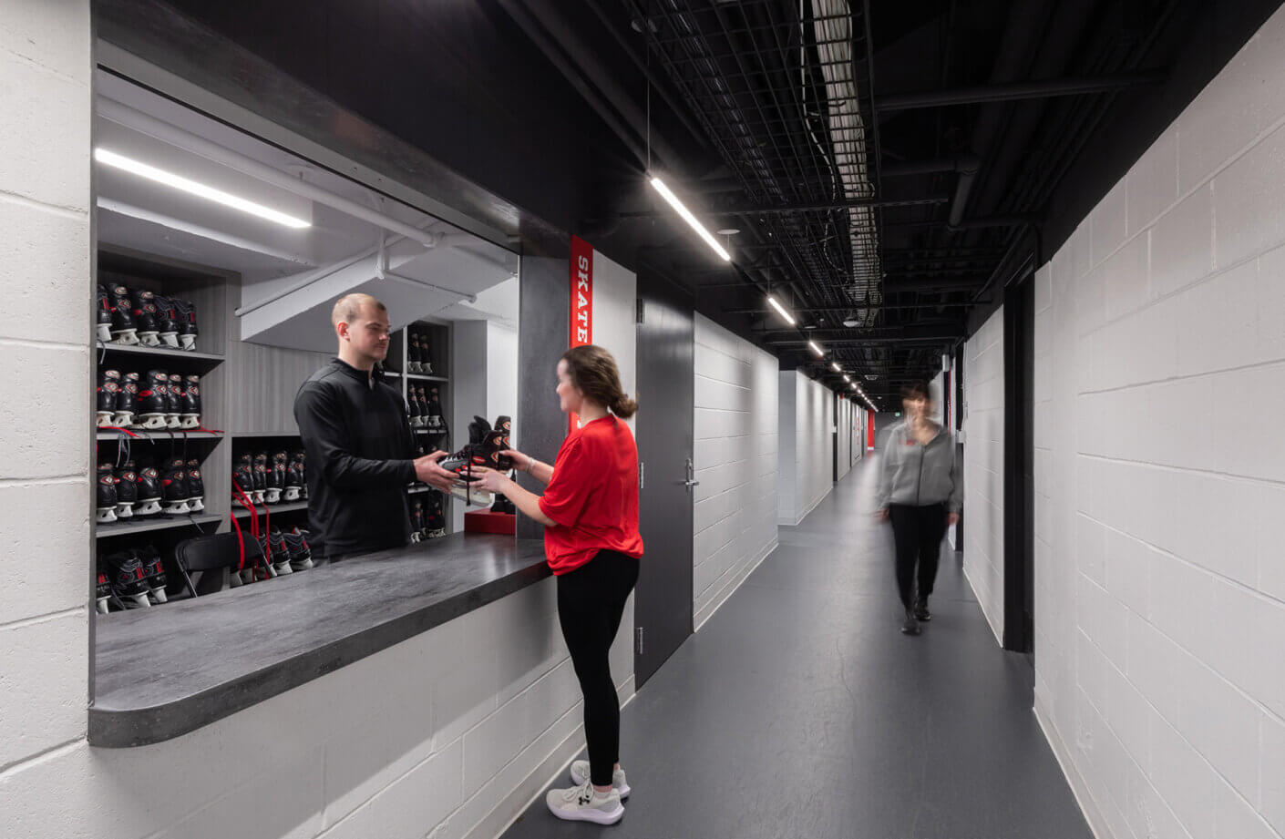 Ice rink skate rental counter with skates and two people exchanging equipment.