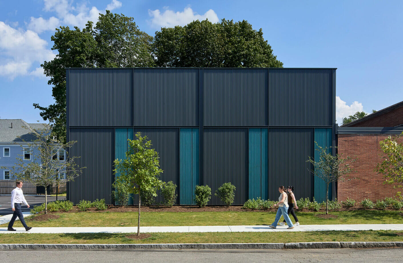 Contemporary community squash center building facade with trees and pedestrians on sunny day.