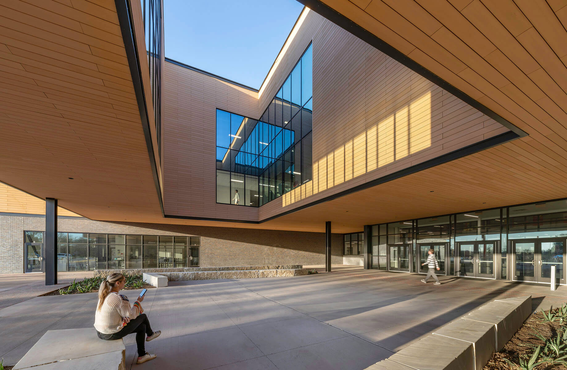 Modern building exterior with glass windows; woman seated outside on phone.