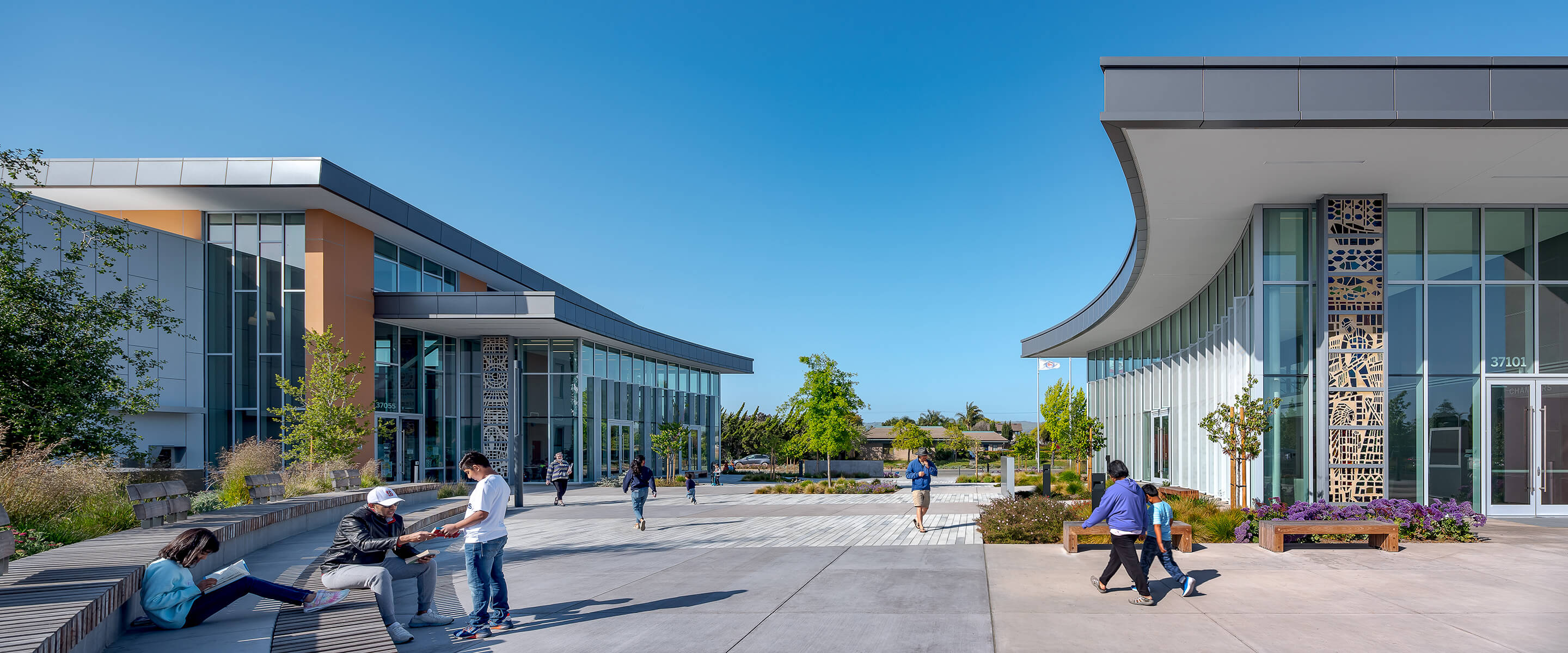 Modern campus courtyard with people walking and seating under a clear blue sky.