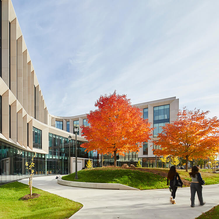 Modern campus building with vibrant autumn trees and walking people.