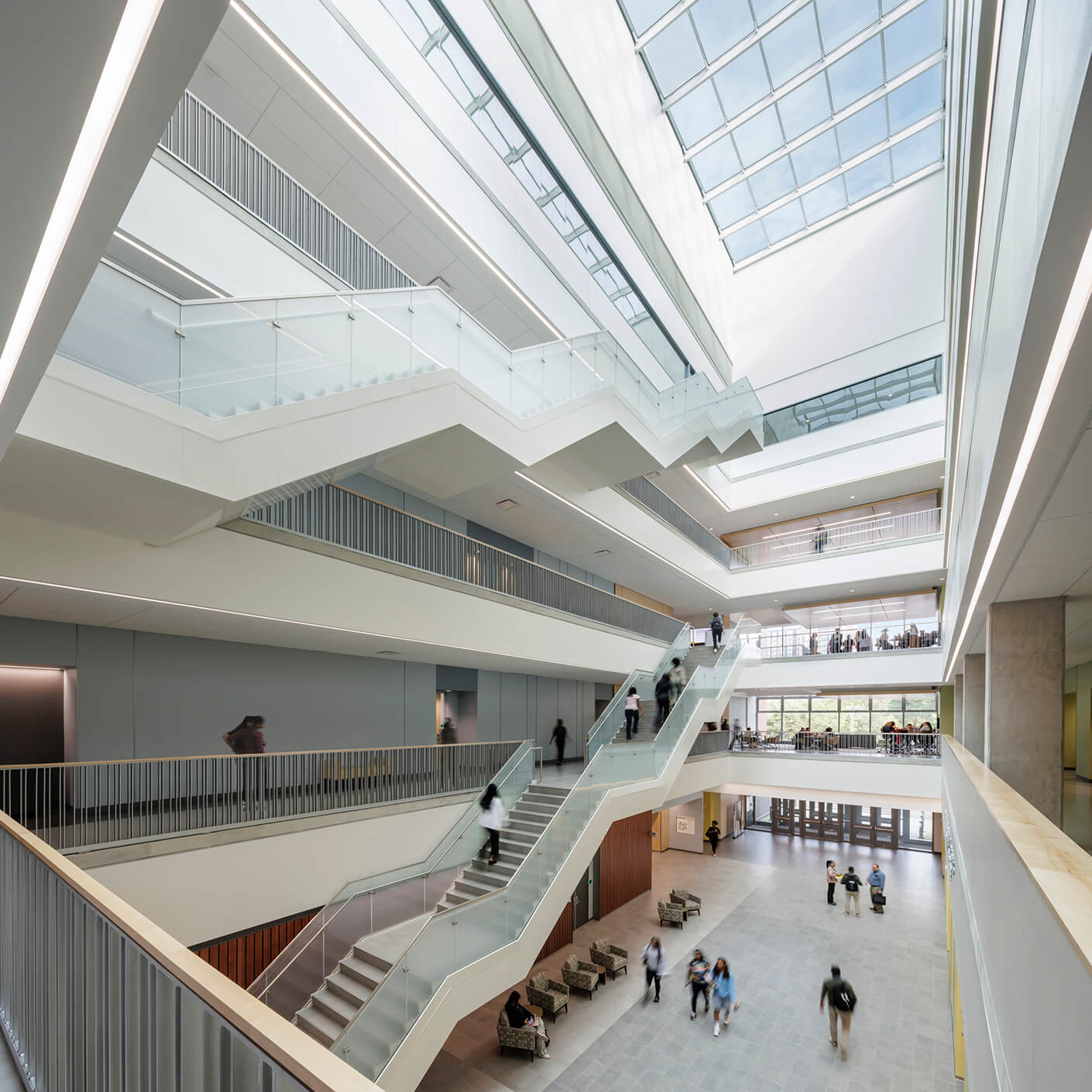 Modern atrium with glass ceiling and busy staircases in a multi-level building interior.