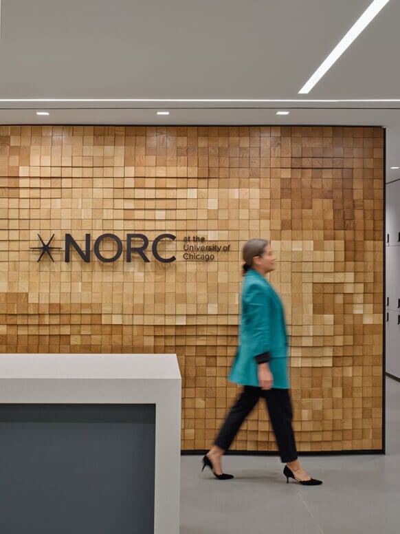 Person walking past NORC University of Chicago sign on wooden wall.