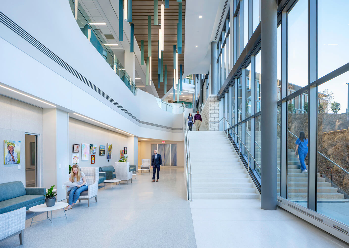Modern hospital lobby with stairs, art, people relaxing.