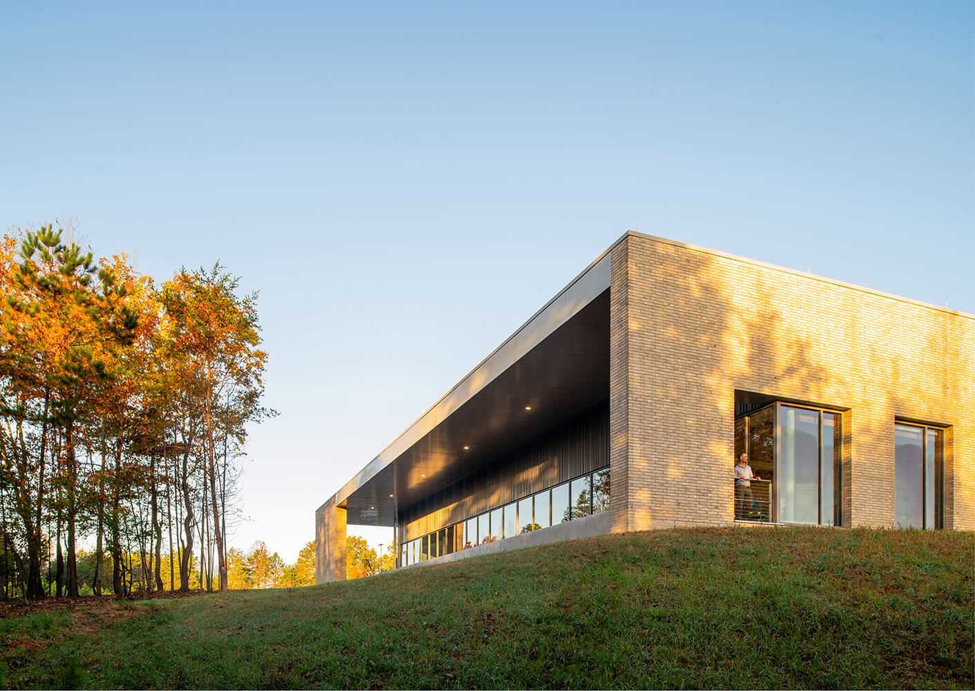 Modern building with large windows surrounded by green lawn and trees at sunset.