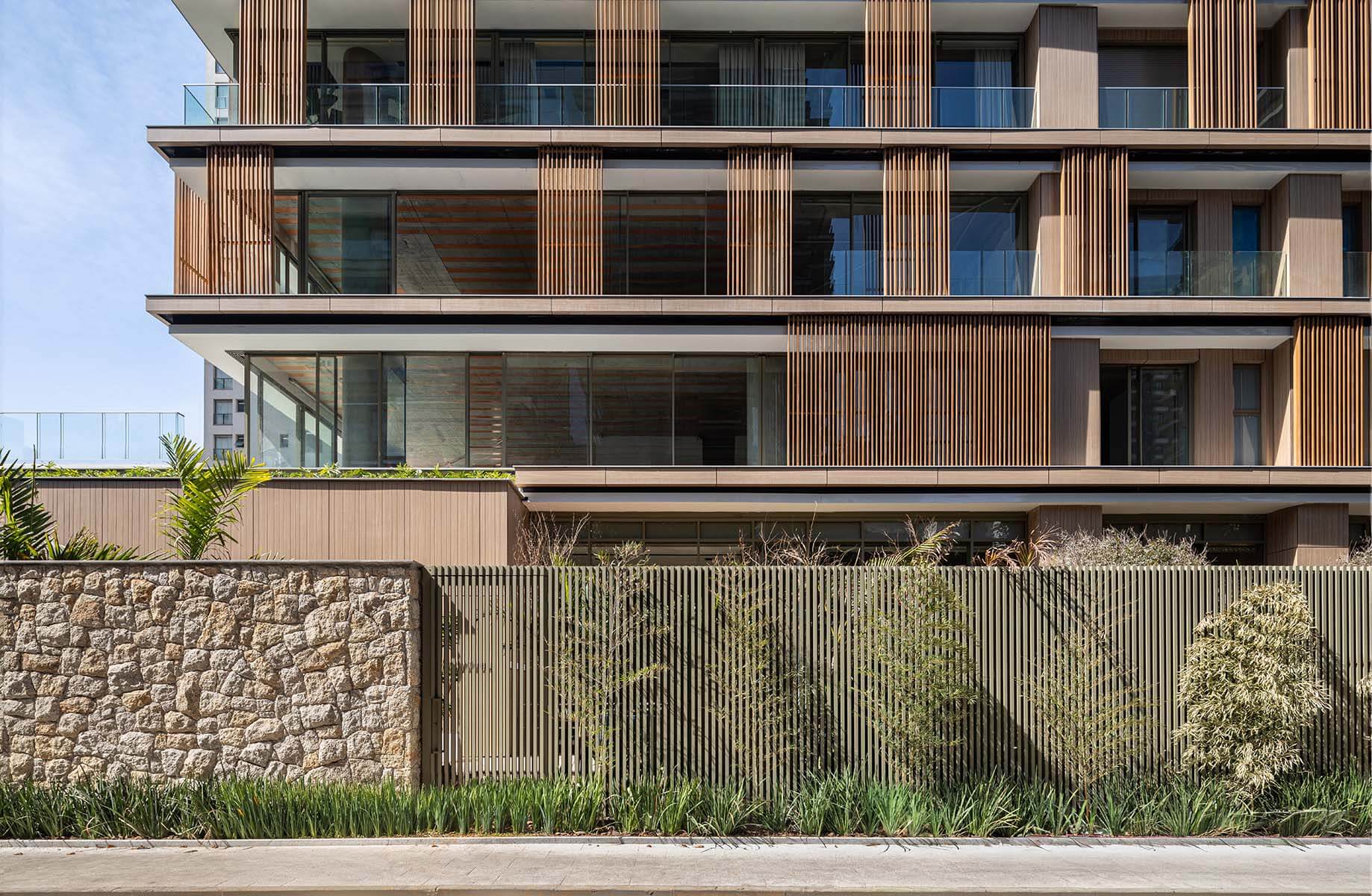 Modern building facade with wooden panels and stone wall, featuring greenery in front.
