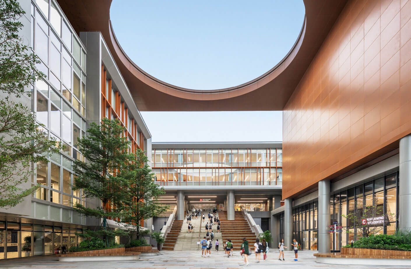 Modern architectural courtyard with people and staircase under circular roof opening.
