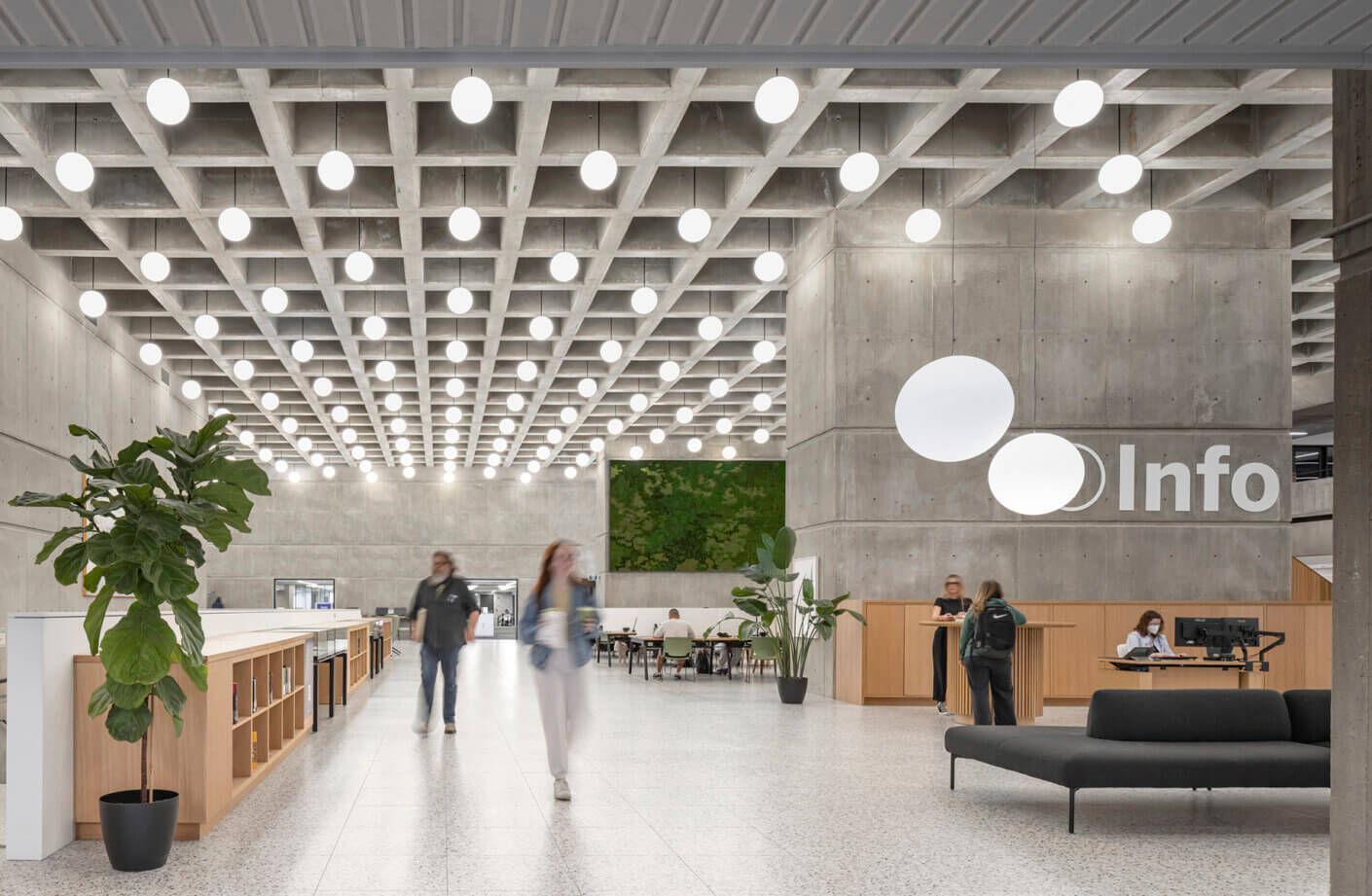 Modern lobby with concrete design, info desk, plants, and bright overhead lights.