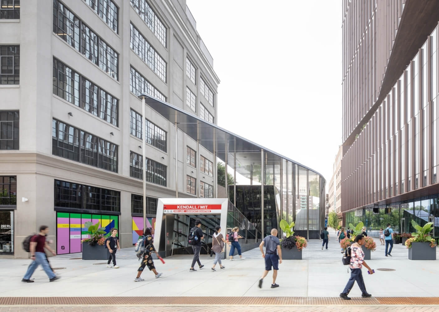People walking near Kendall/MIT station entrance in modern urban area.