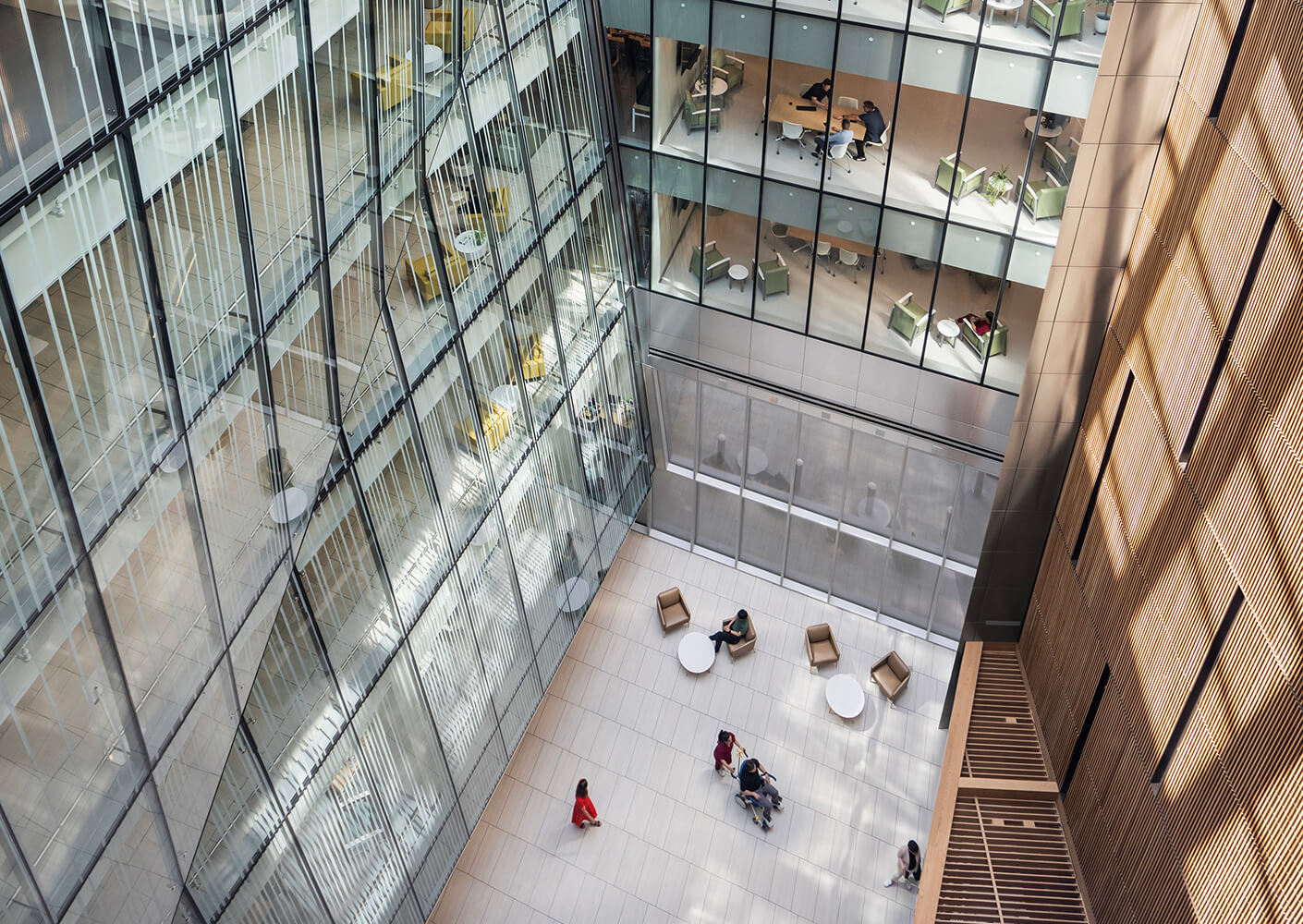 Modern office atrium with glass walls, people gathered around circular tables.