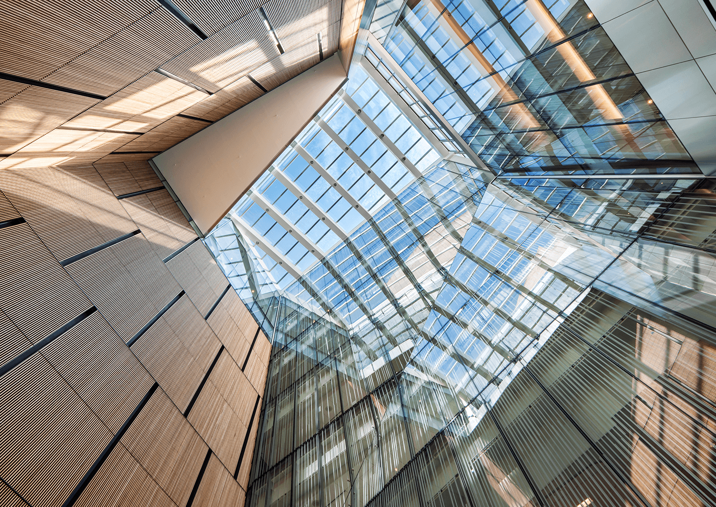 Modern building's glass ceiling viewed from below, showcasing sky and architectural lines.