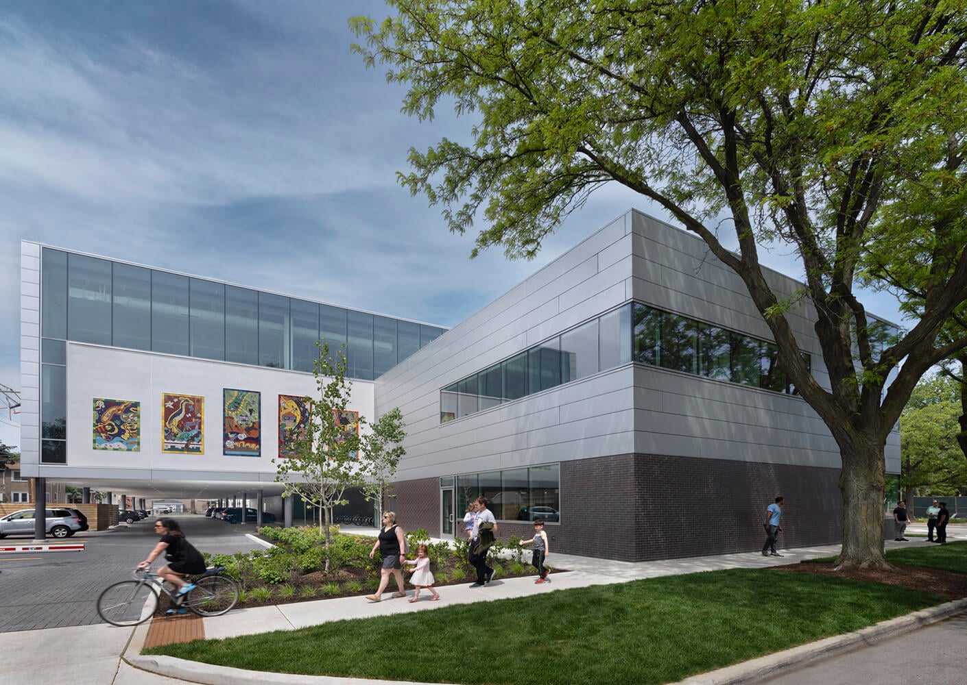 Modern building with people outside, tree and bike path under clear sky.