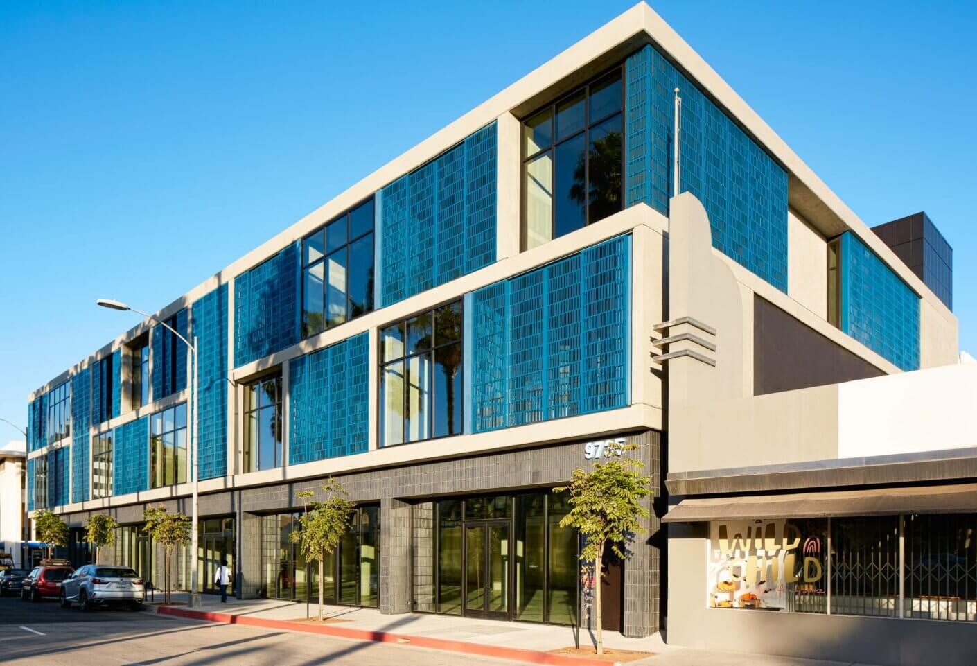 Modern building with blue glass facade and street view on a sunny day.