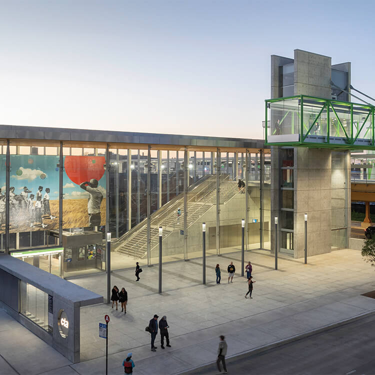 Modern transit station with glass facade and vibrant mural at dusk.