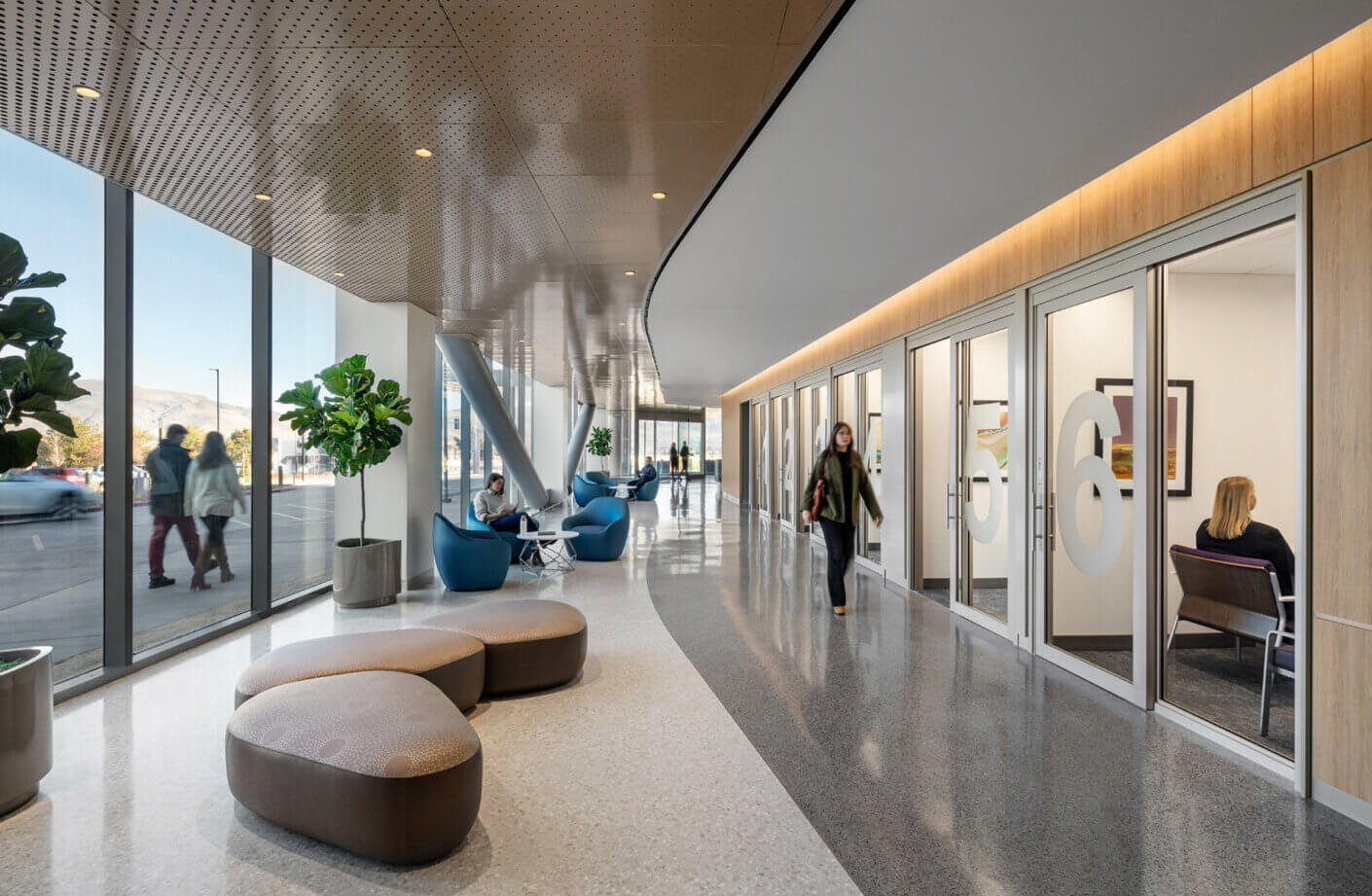 Modern corridor with seating, large windows, and plants.