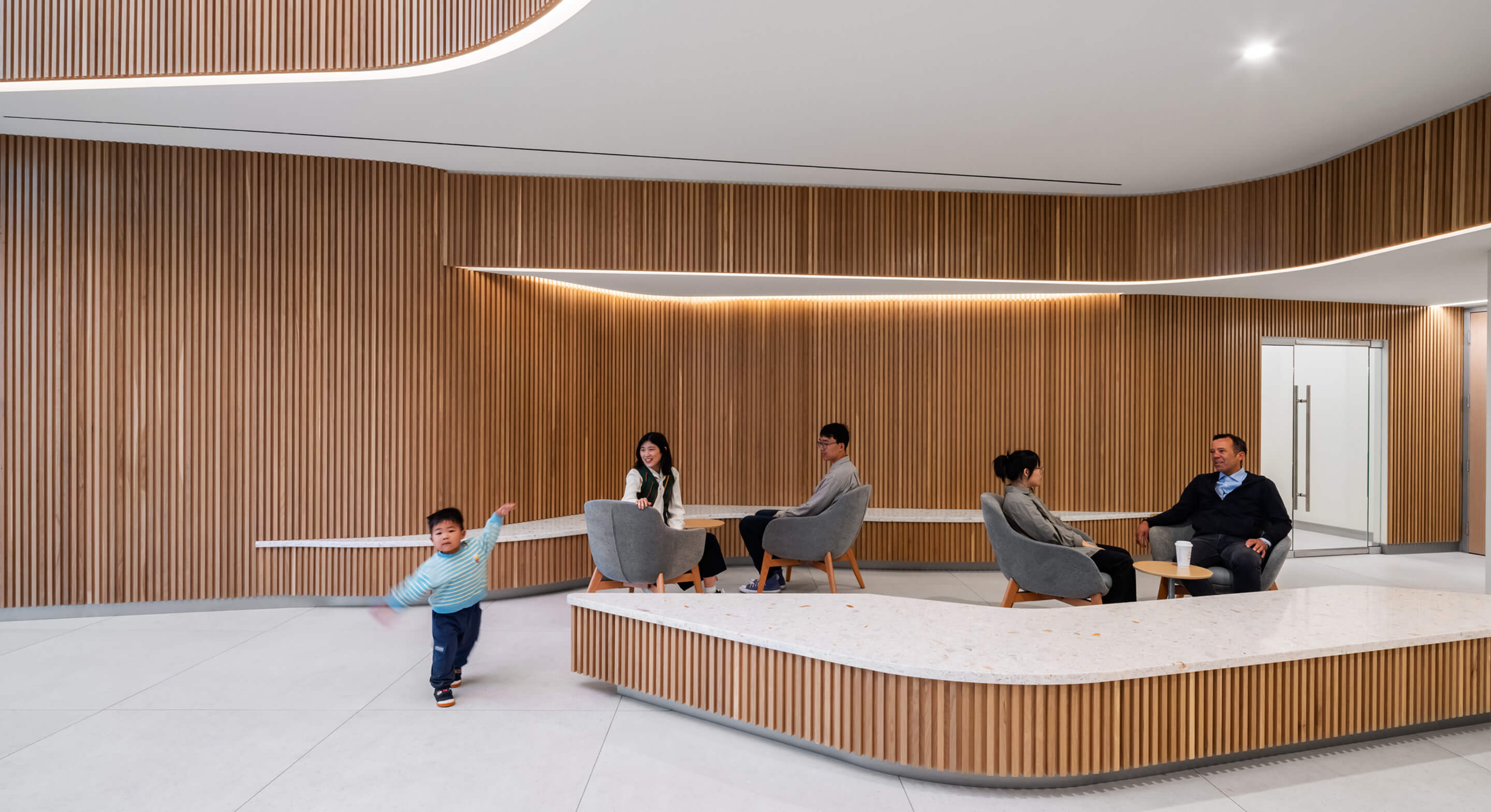 Modern lobby with wooden walls, people sitting, and a child playing.