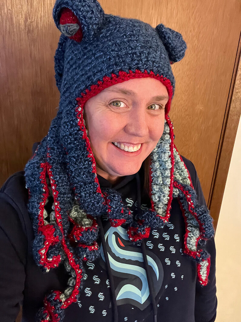 Sarah wearing blue knit hat with bear ears and matching hoodie, smiling at camera.