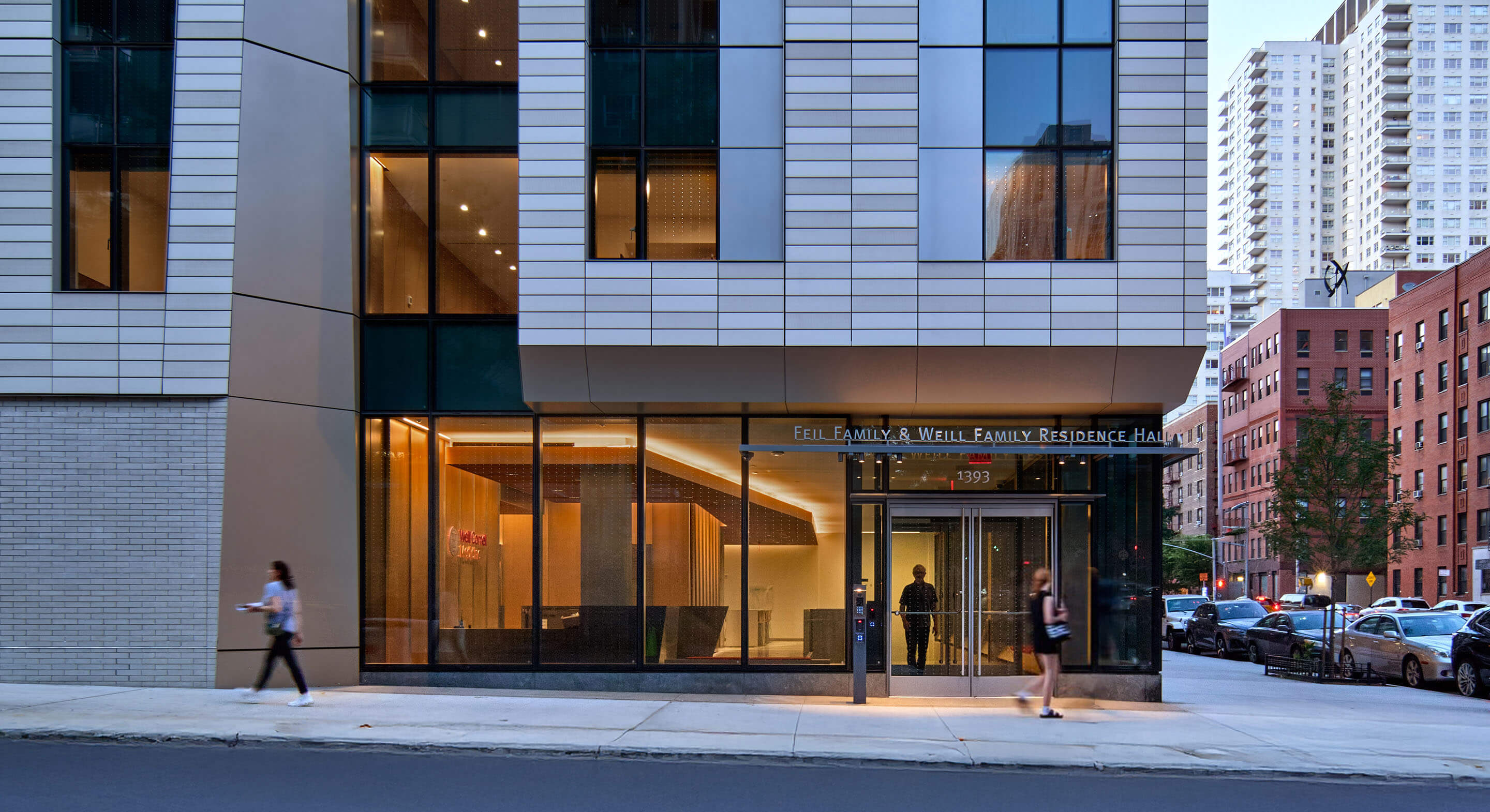 Student residence building with glass windows and street view at dusk.