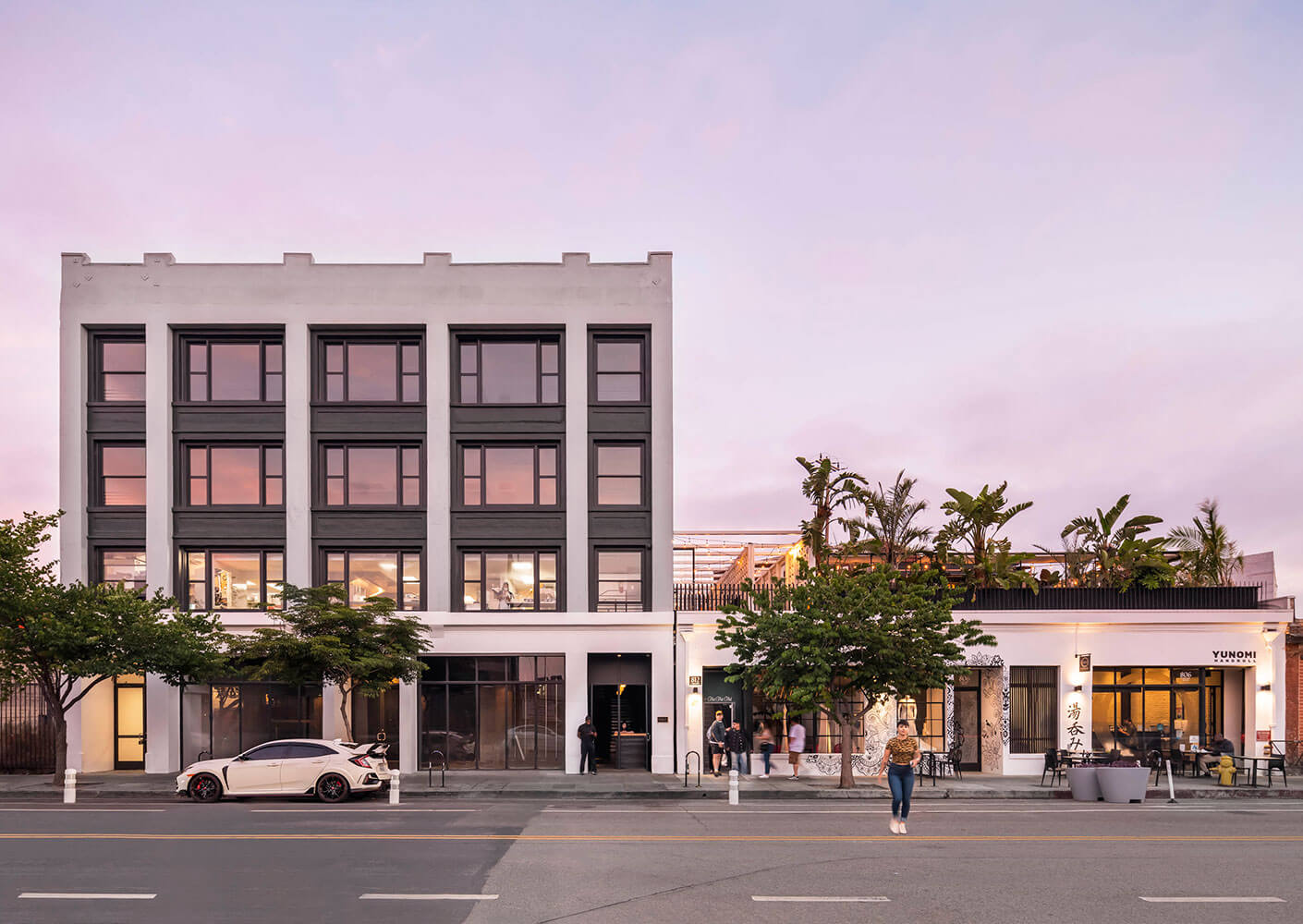 Modern building facade at sunset with trees and parked cars.