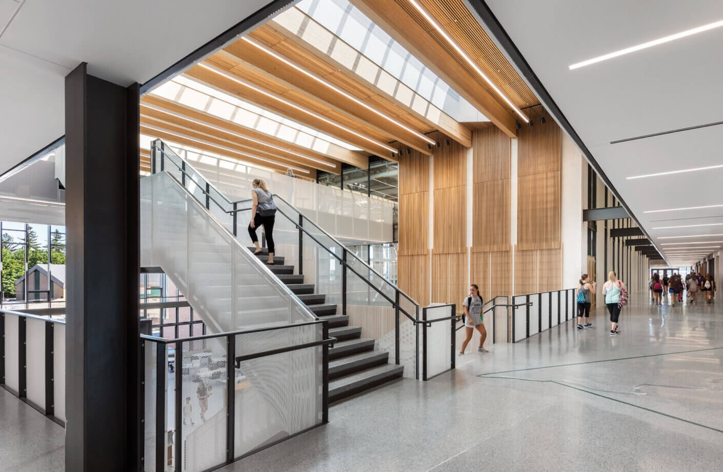 Modern interior with staircase and skylight, people walking in bright, open space.
