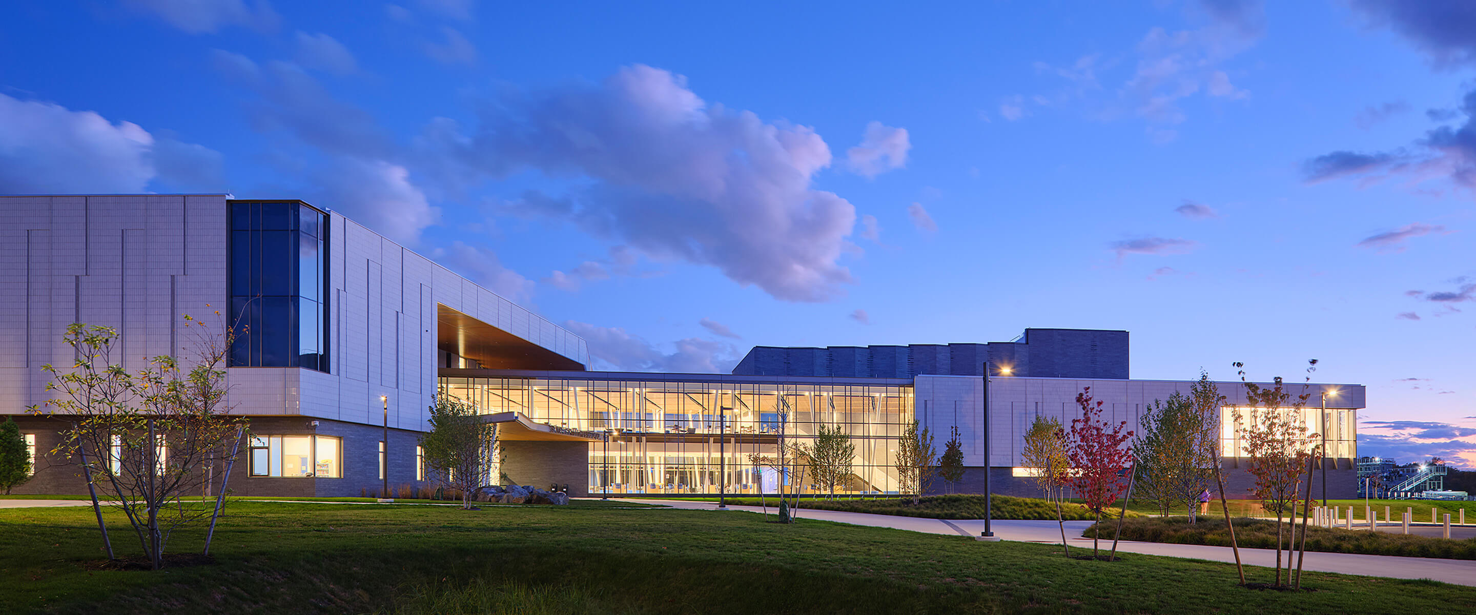 Modern building exterior at dusk with lush landscaping and dramatic cloud sky.